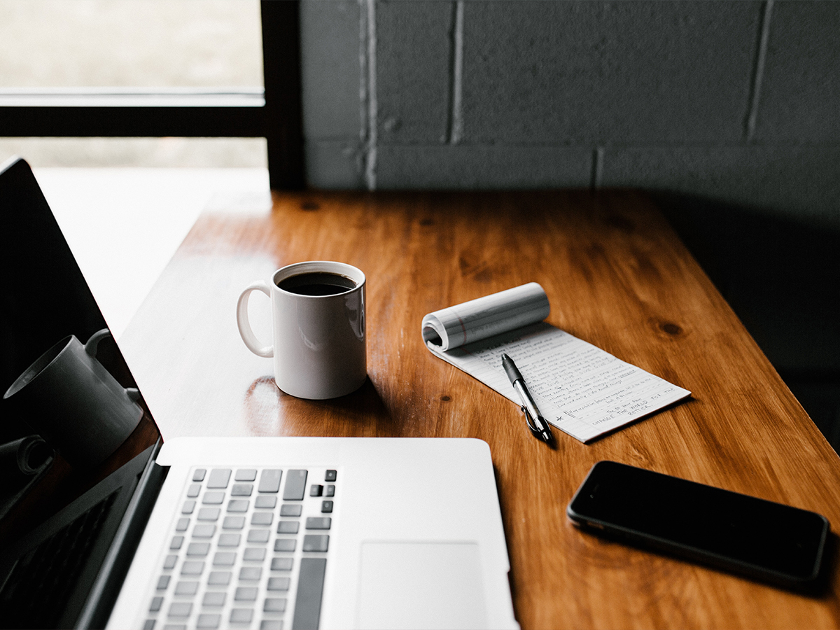 laptop, smartphone, coffee, and pen and pad of paper sitting on a desk