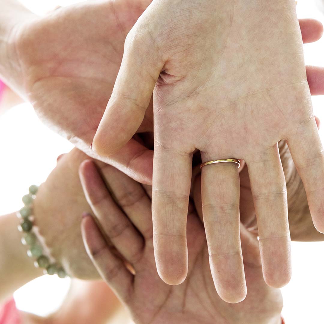 People with their hands together in a circle preparing to contribute to their community.