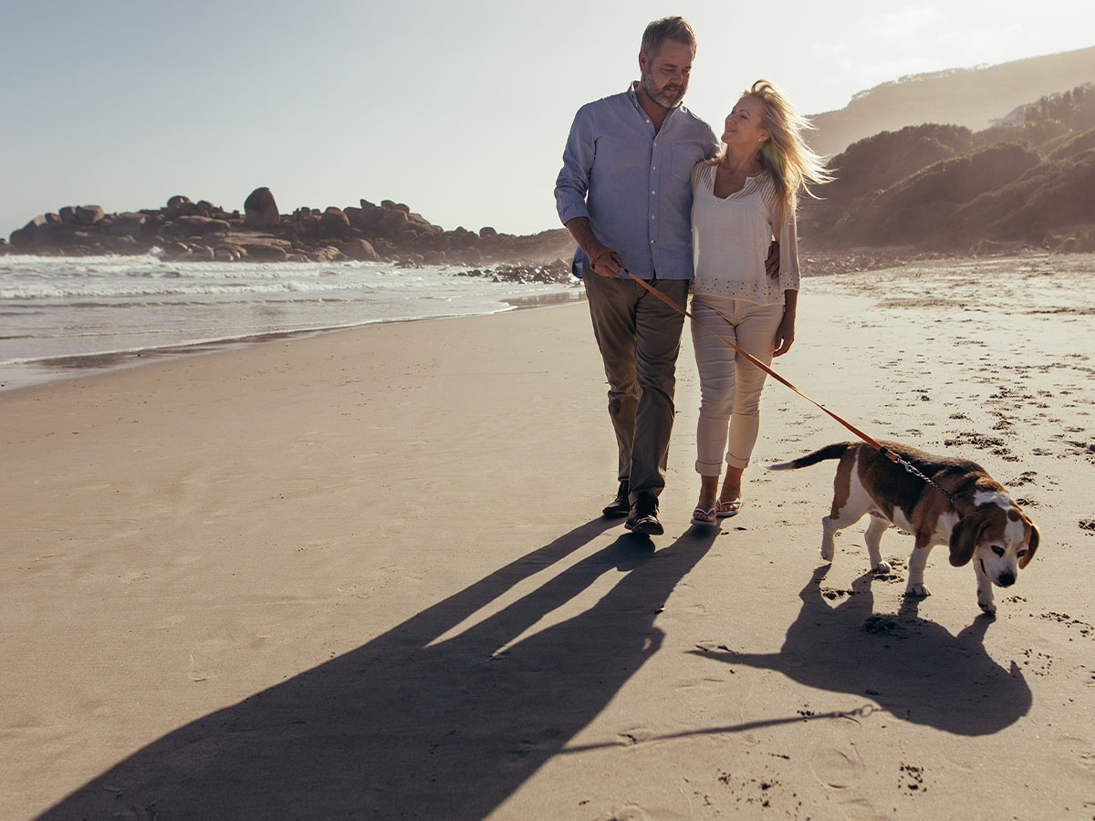 Couple walking their dog on the beach.