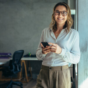 A young woman holds her phone and smiles
