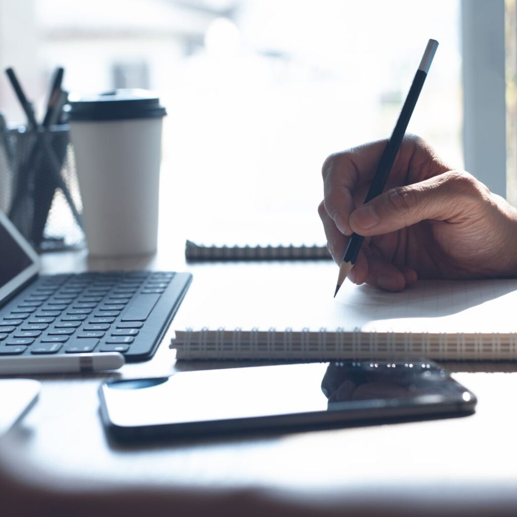 image of a computer keyboard, and someone holding a pencil poised over a notepad